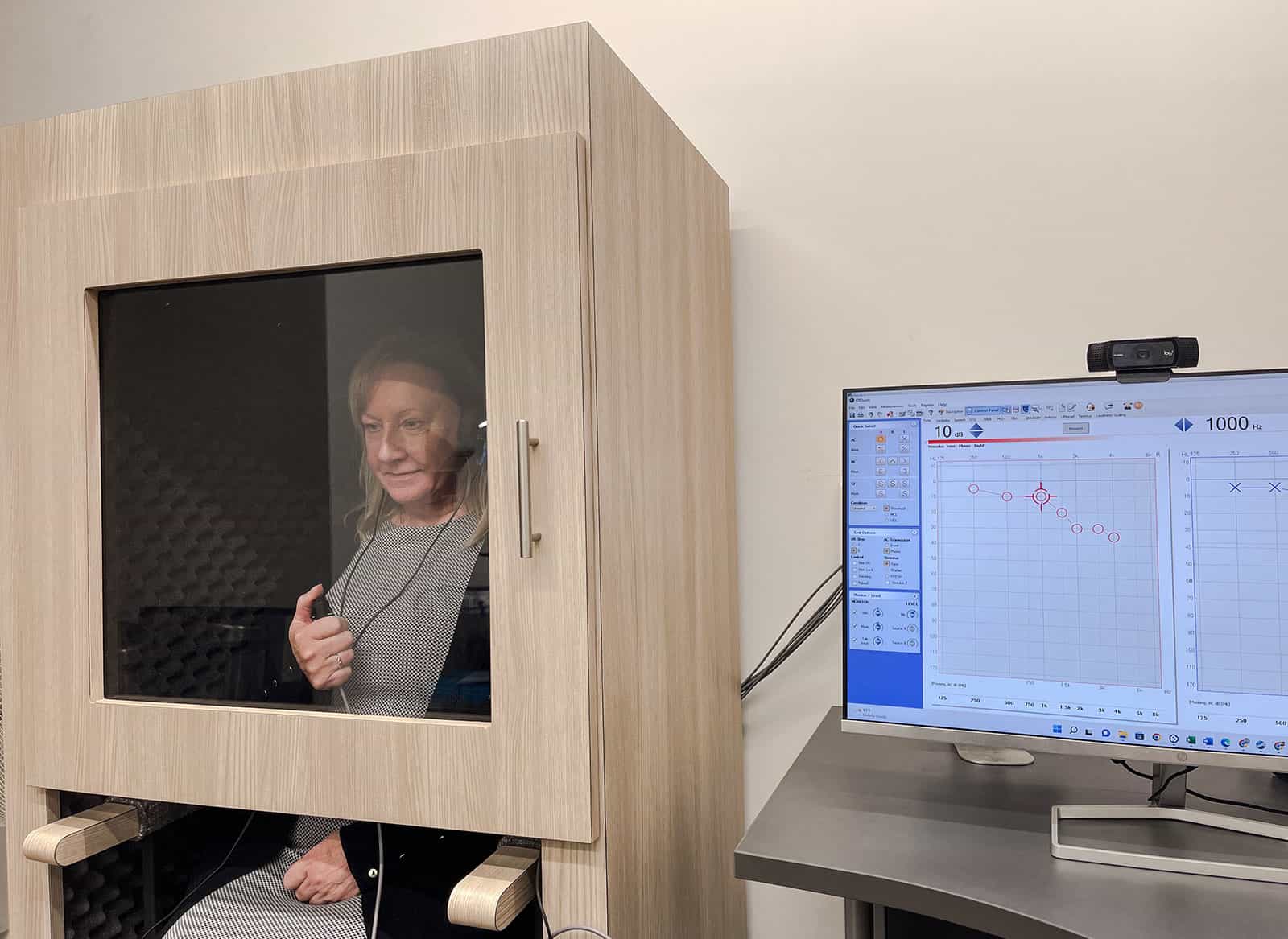 Lady in sound proof booth completing a hearing test